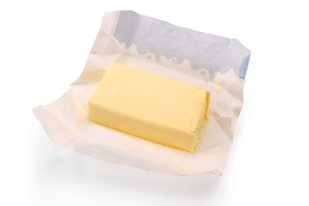 Unpacked block of butter on wax paper from packaging, isolated on white, clipping path included