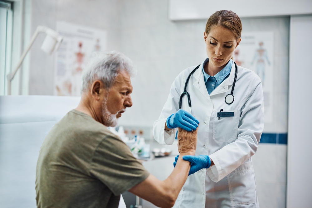 Female physical therapists checking senior patient's hand at medical clinic.