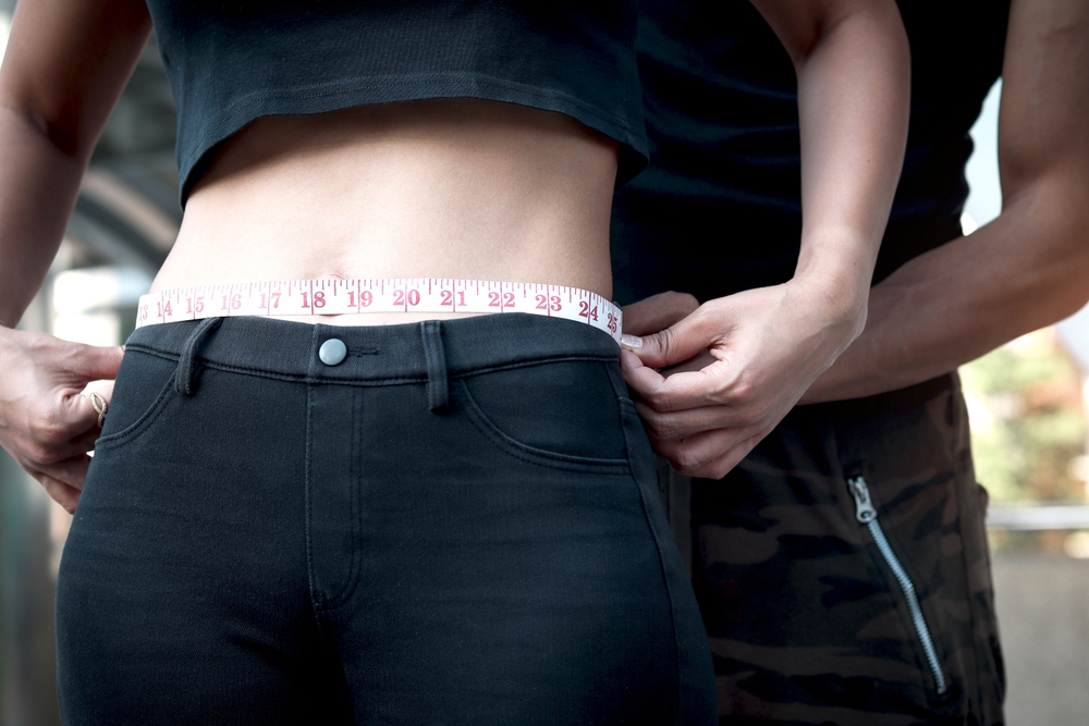 Slim young sport girl measuring her thin waist with tape measure, her exercise partner trainer helping her to measure her waist, successful results from exercise, lose weight, strong body and healthy
