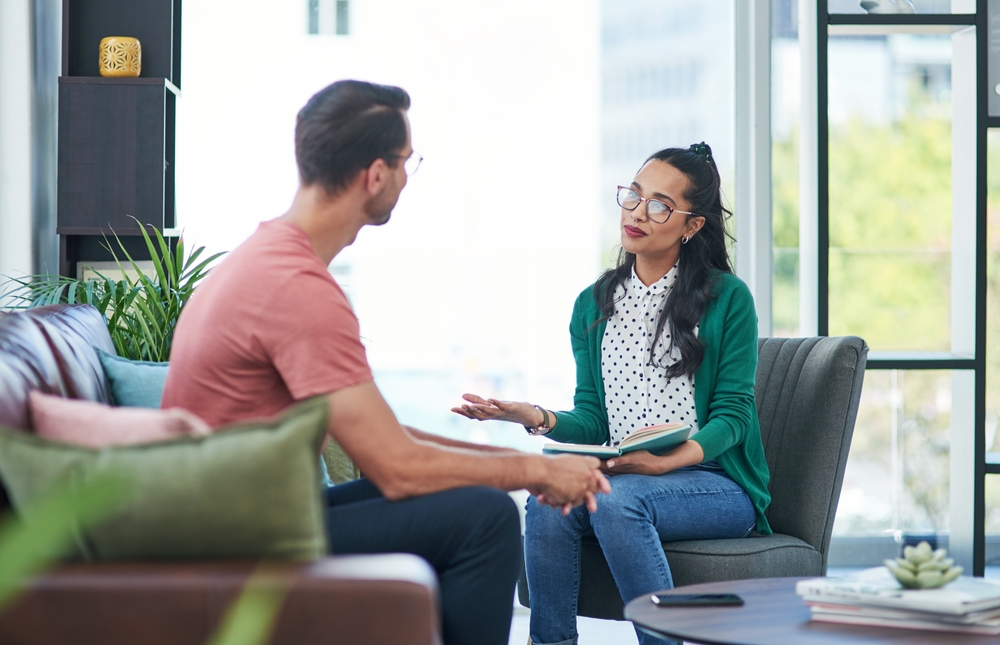 Mental health, therapy or counseling with a woman psychologist and male patient talking in her office. Psychology, wellness and trust with a female doctor or shrink consulting a man for healing
