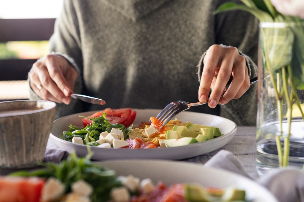 Woman eating healthy morning meal. Healthy breakfast with salmon, omelet, avocado, fresh herbs, cheese and tomatoes