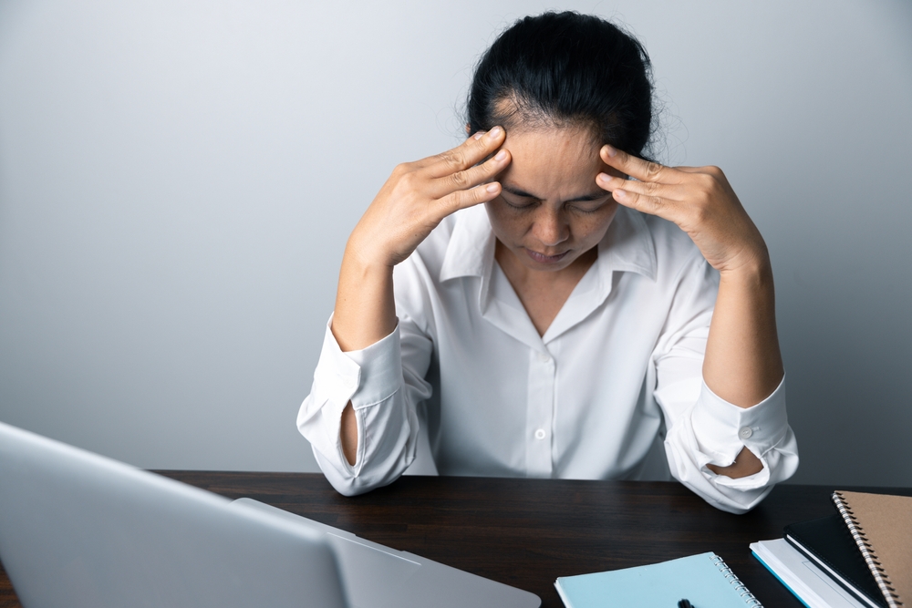 A business office worker is an asian woman is sitting in front of the laptop computer. A businesswoman stressing her body part fingers, hands arm. A femaleOffice manager is exhausted at her workplace.