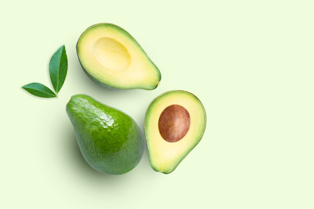 Avocado fruit and cut in half sliced with green leaf isolated on green color background. Top view. Flat lay. Copy space.