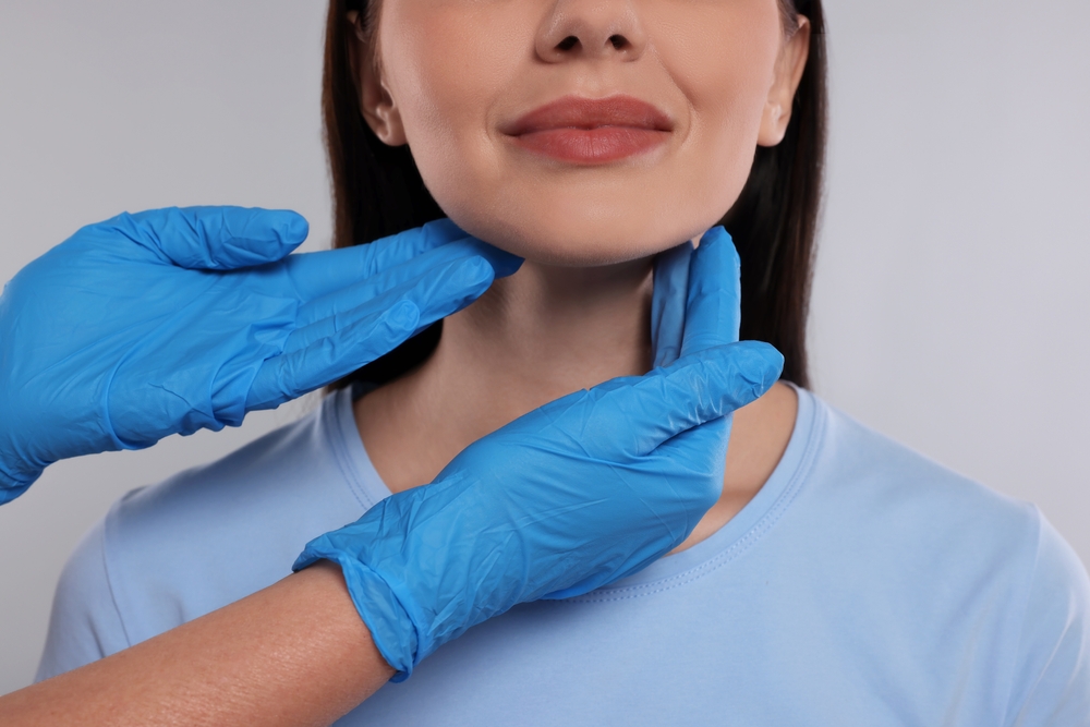 Endocrinologist examining thyroid gland of patient on light grey background, closeup