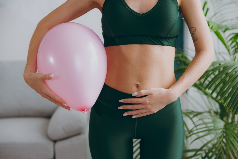 Cropped close up young strong sporty athletic fitness trainer instructor woman wear green tracksuit training hold balloon near belly do exercises at home gym indoor. Workout sport motivation concept