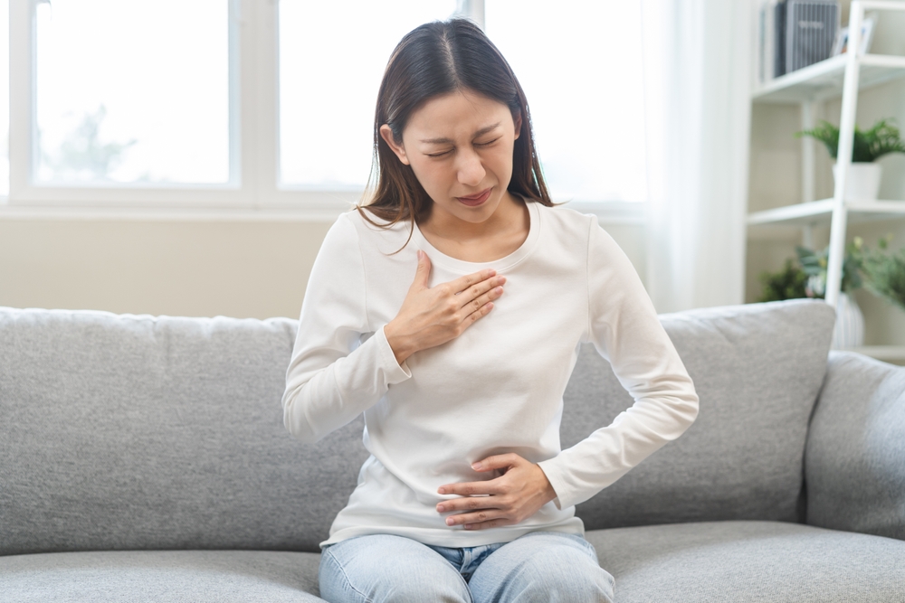 Acid reflux disease, suffer asian young woman have symptom gastroesophageal, esophageal, stomach ache and heartburn pain hand on chest from digestion problem after eat food, Healthcare medical concept
