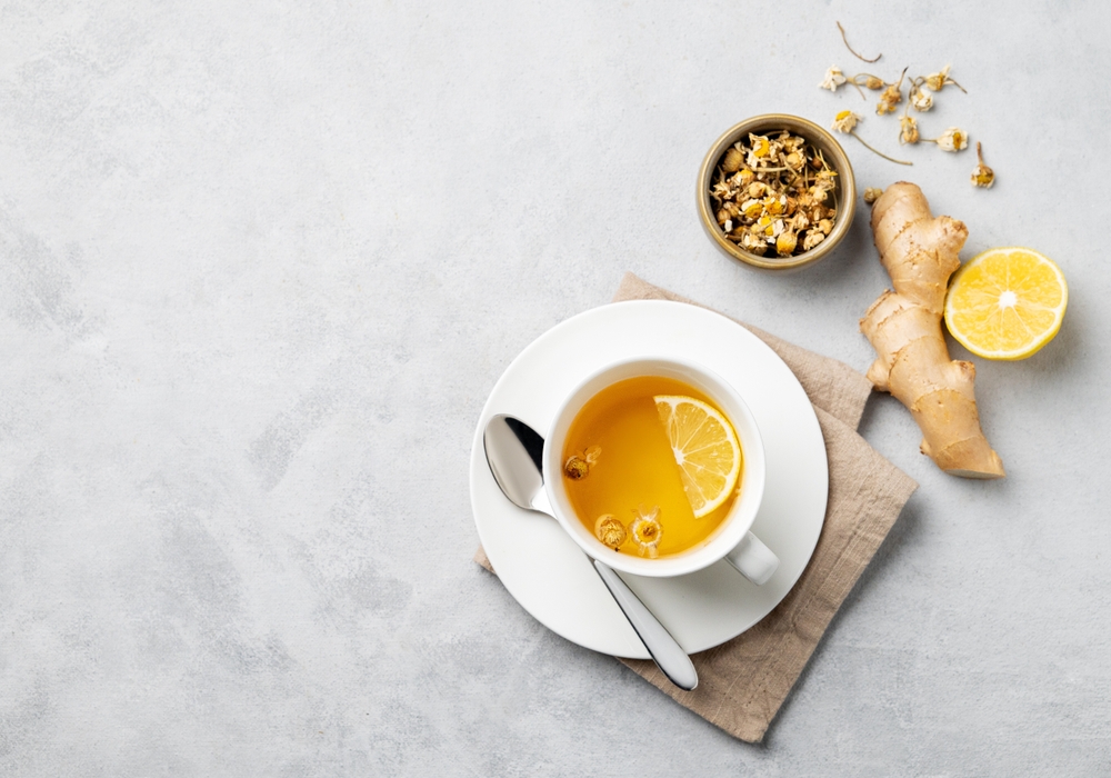 Chamomile herbal tea with lemon in a white cup on a light background with dry flowers and ginger. The concept of a healthy detox drink for health and immunity. Top view and copy space.