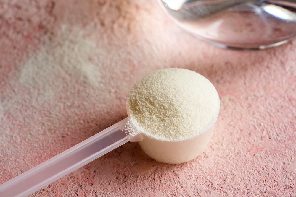 Collagen powder in a plastic measuring cup on pink background next to a glass of water