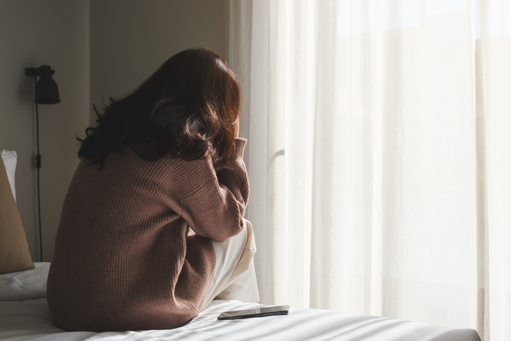Rear view of a sad woman after reading bad news on smartphone in bedroom