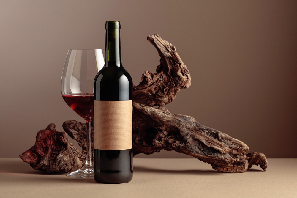Bottle and glass of red wine. On a bottle old empty label. In the background old weathered snag. Frontal view with copy space.