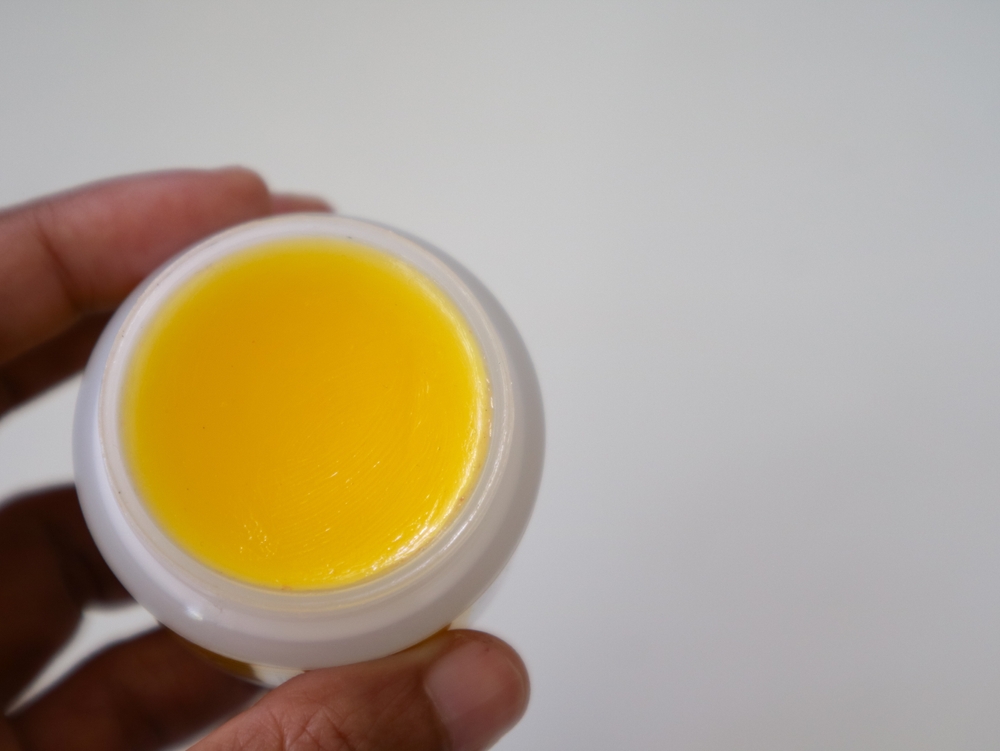 hand holding natural lip balm from beeswax in tin circle jar.