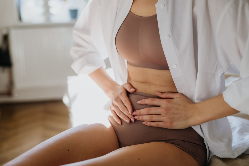 Woman at home suffering from menstrual pain, having cramps. Close up of woman holding abdomen, endometriosis, and conditions causing pain in tummy.
