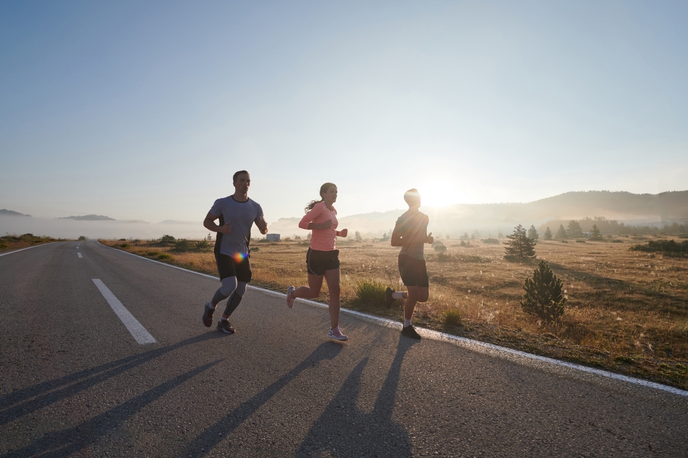 A group of friends, athletes, and joggers embrace the early morning hours as they run through the misty dawn, energized by the rising sun and surrounded by the tranquil beauty of nature