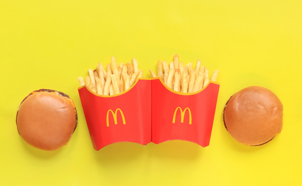Kyiv, Ukraine - January 31, 2024: French fries in paper packaging and cheeseburgers on a yellow background, top view. McDonald's Corporation is the world's largest fast food restaurant. Copy space