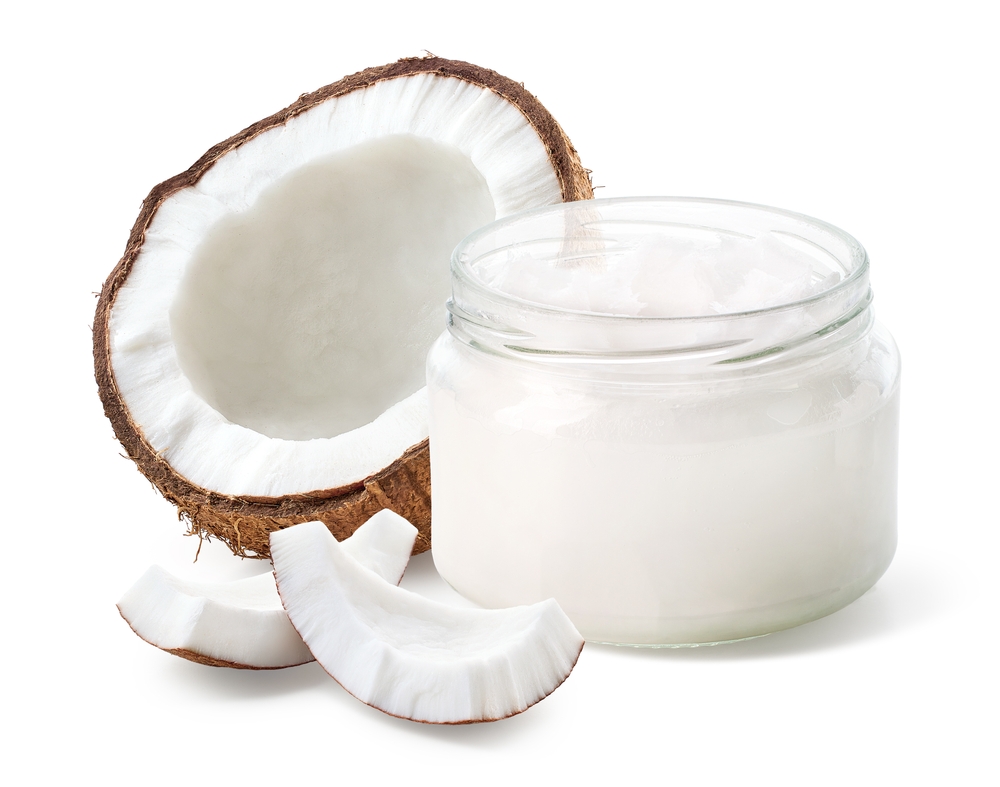 Open glass jar of coconut oil and fresh coconut halve and pieces isolated on white background