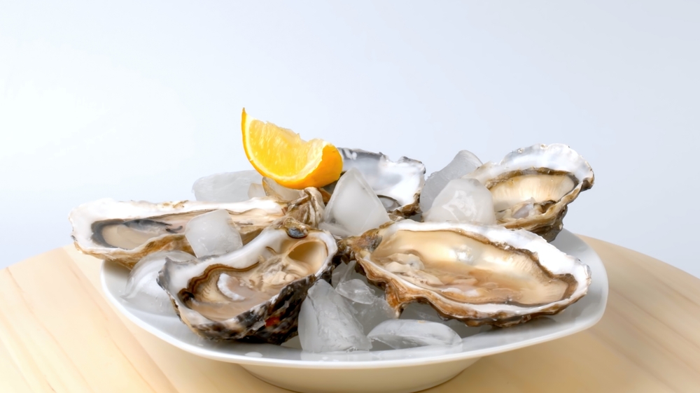 A plate of oysters with lemon on a gray background. Served with oysters and lemon. Fresh oysters close up. Healthy sea food. Oyster dinner in a restaurant. Oysters with lemon.