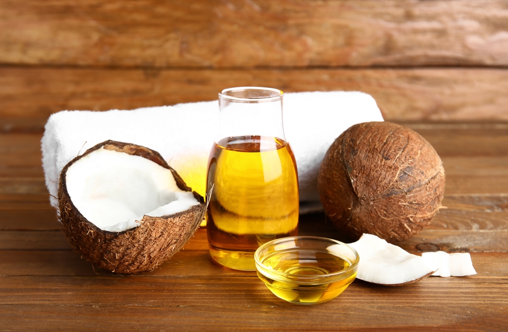 Bottle and bowl of coconut cosmetic oil and bath towel on brown wooden background