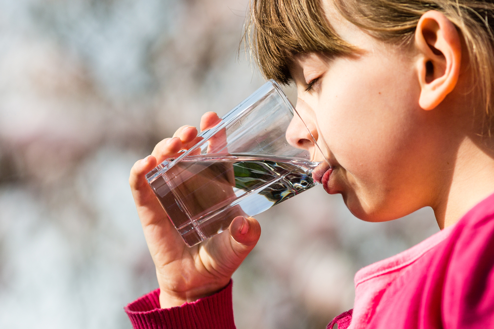 Young girl holding glass and drinking pure water. Ideal for environmental protection or future generations concept.