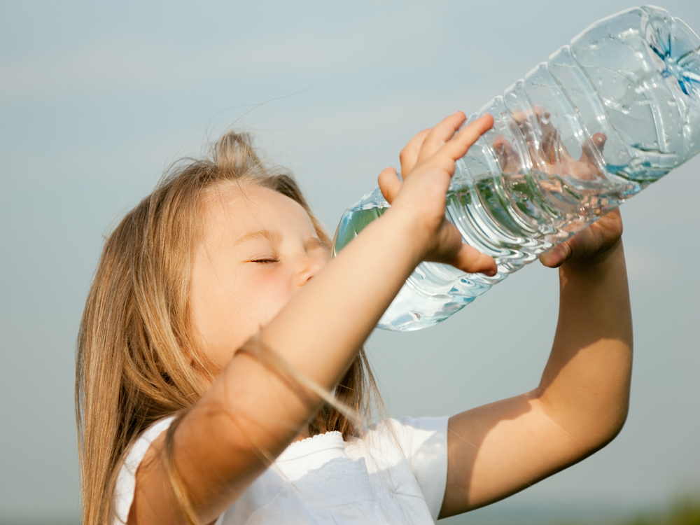Kid drinking water from a bottle against a sky background