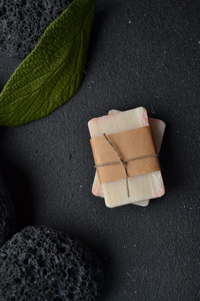 Bars of soap wrapped natural brown paper. With leaves, pumice, and black stone in the background.