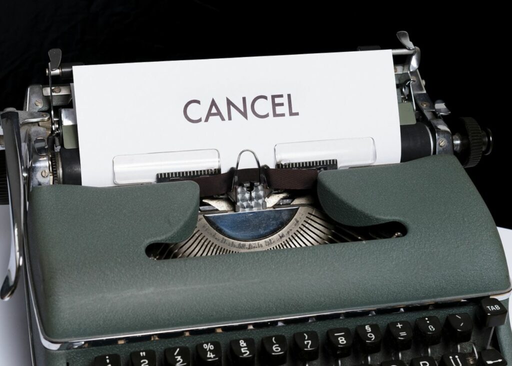 A green typewriter with the word "cancel" on a piece of paper. Black background. 