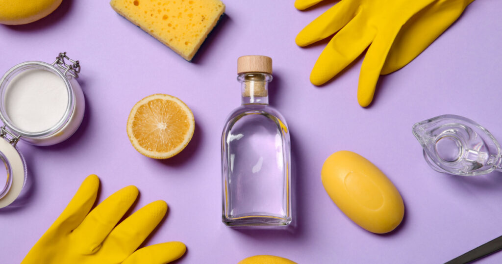 Flat lay composition with vinegar and cleaning supplies on color background