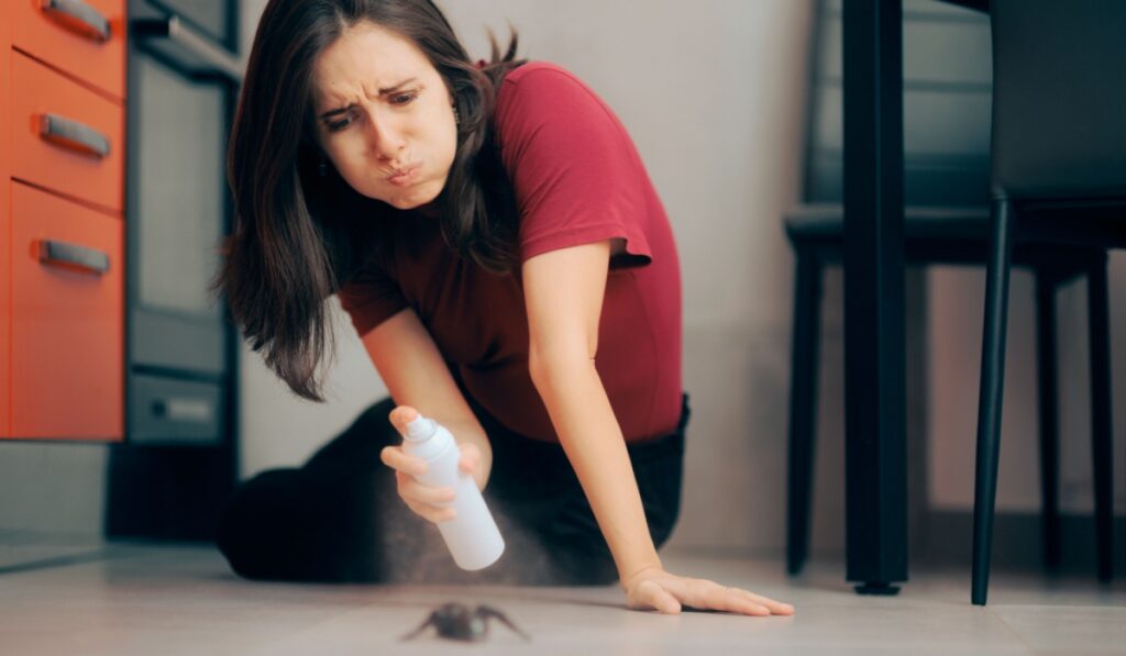 Woman Spraying with Insecticide Over an Ant on the Kitchen Floor. Homeowner dealing with pest infestation problem in her own apparent