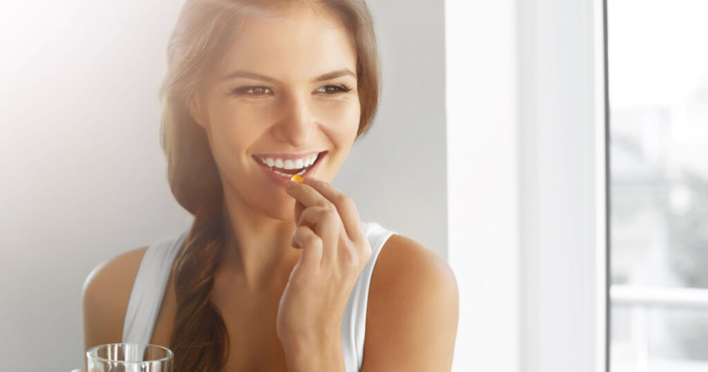 Diet. Nutrition. Healthy Eating, Lifestyle. Close Up Of Happy Smiling Woman Taking Pill With Cod Liver Oil Omega-3 And Holding A Glass Of Fresh Water In Morning. Vitamin D, E, A Fish Oil Capsules.