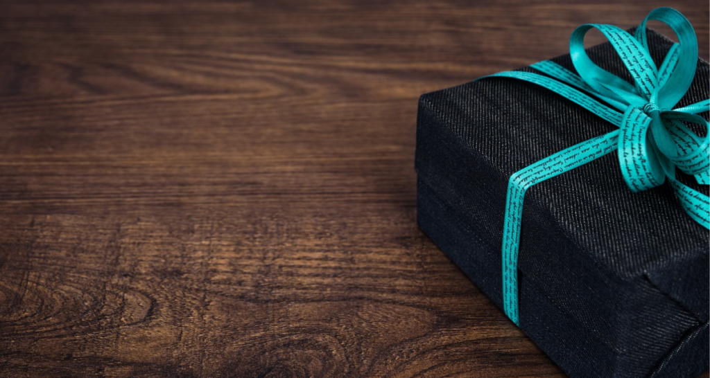 A black box wrapped in a light blue-green ribbon. Wooden background. 