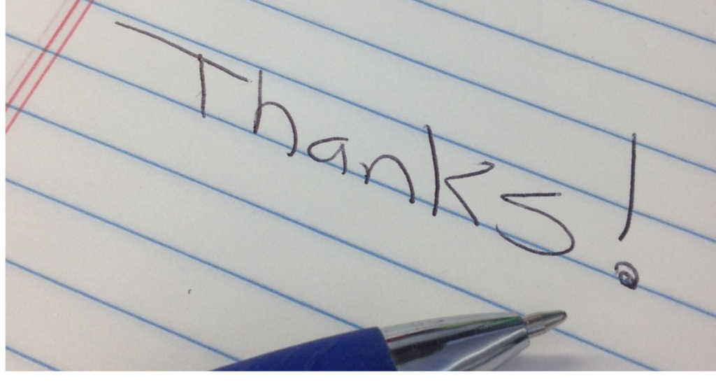 A handwritten note saying "thanks!" on lined paper with the tip of a pen.