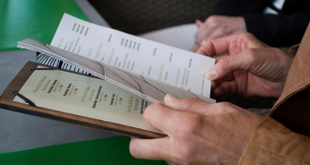 Hands holding a menu at a restaurant table. 