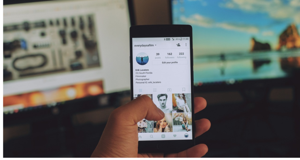 A hand holding a phone. Computers in the background. 