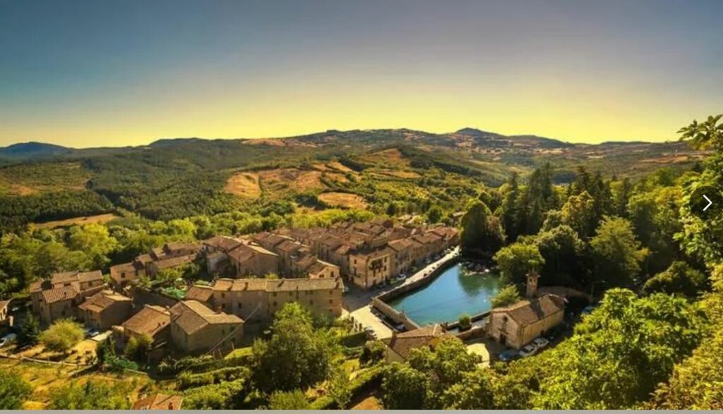Several Tuscan homes on a mountainside. Trees, mountains, and sky in the background.