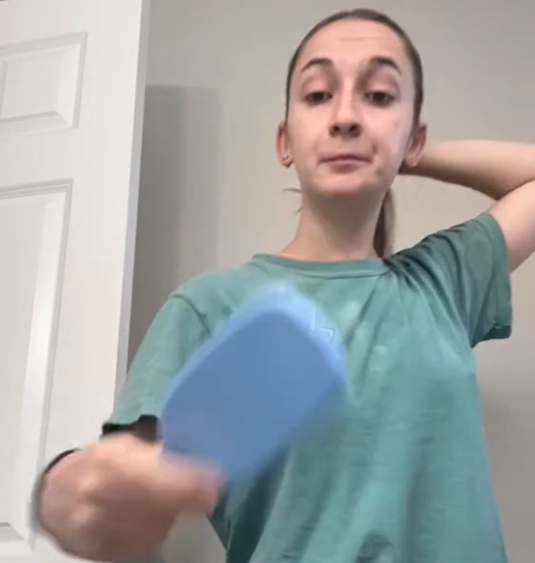 A woman brushing her hair. White walls and door in the background.