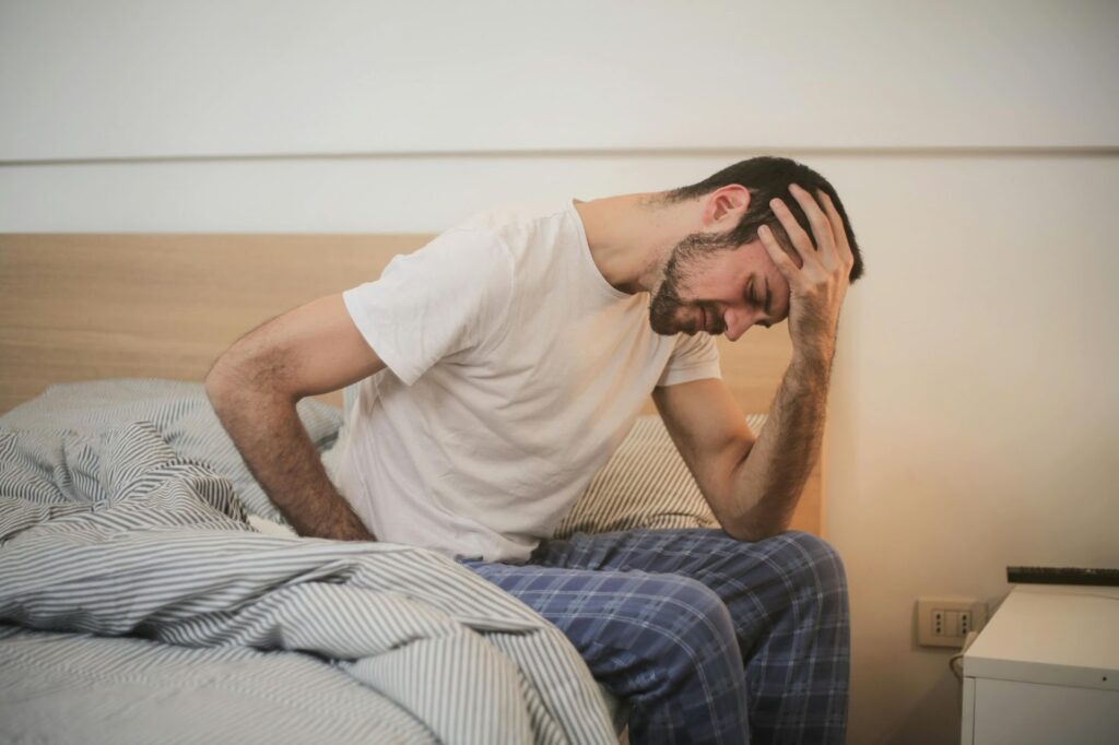 man sitting up in bed with hand placed on head. Illness concept 