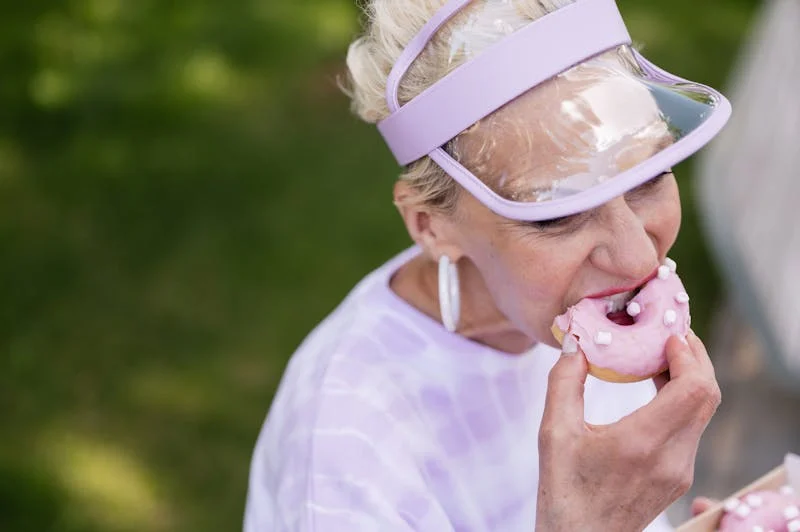 old age woman in a sunhat eating a donut