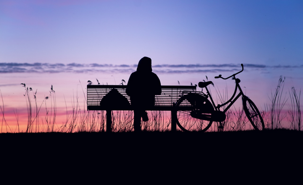 person sitting on a bench with their bike at sunrise