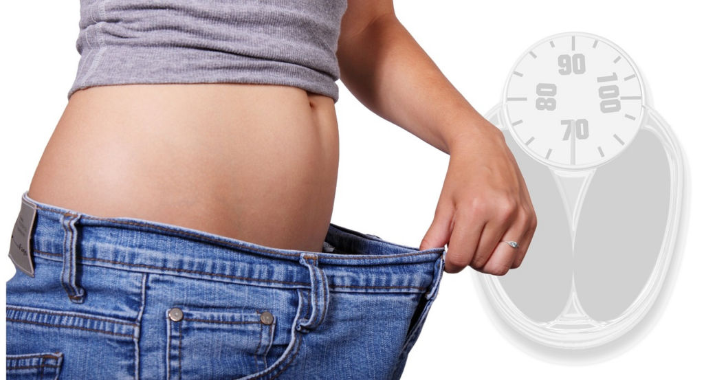 person holding a larger pair of jeans and a scale in the bakcground