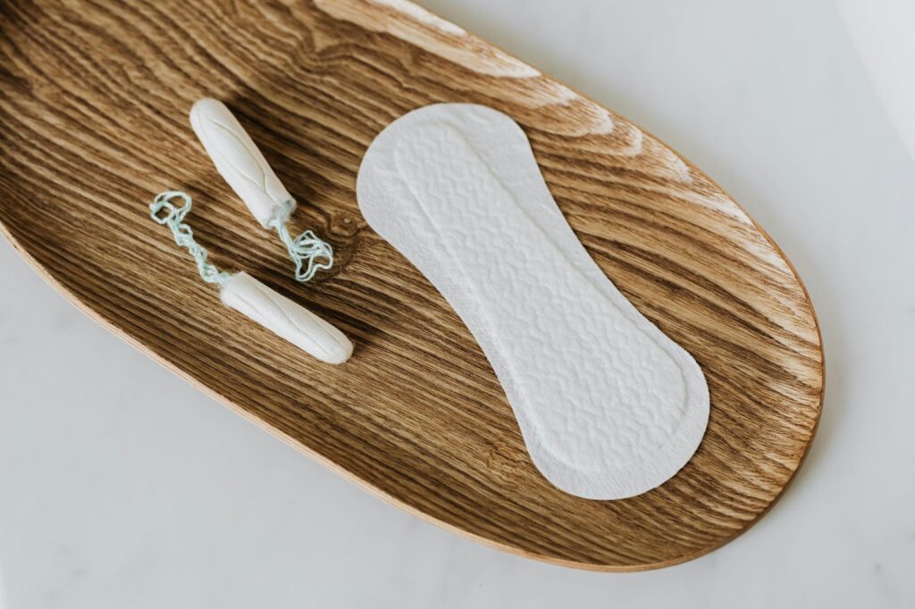 two tampons and a menstrual pad on oval wooden plate 