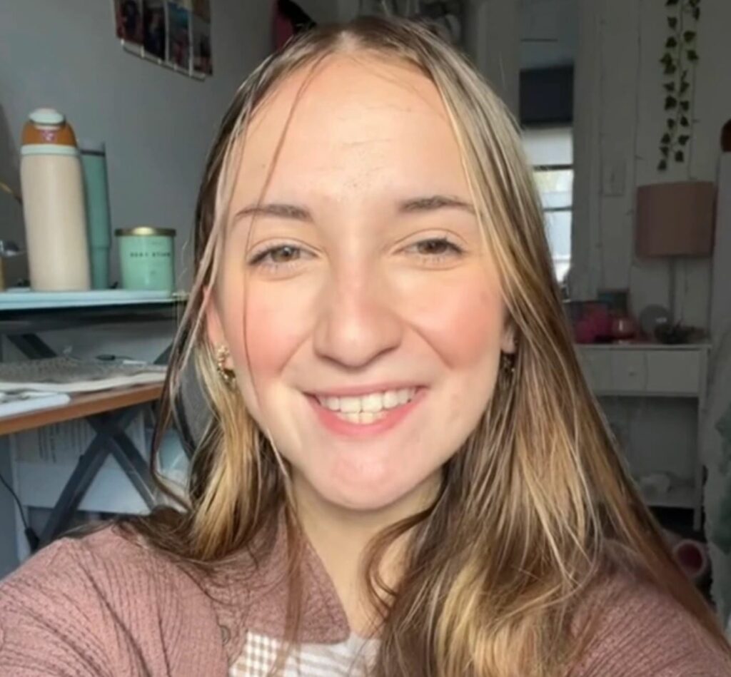 A close-up of a young woman smiling. Kitchen in the background.