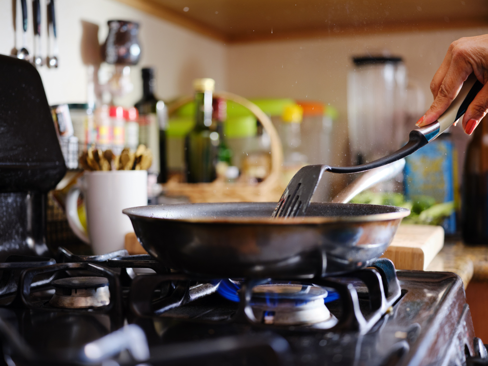 stirring strips of beef in hot skillet inside home kitchen on gas stove