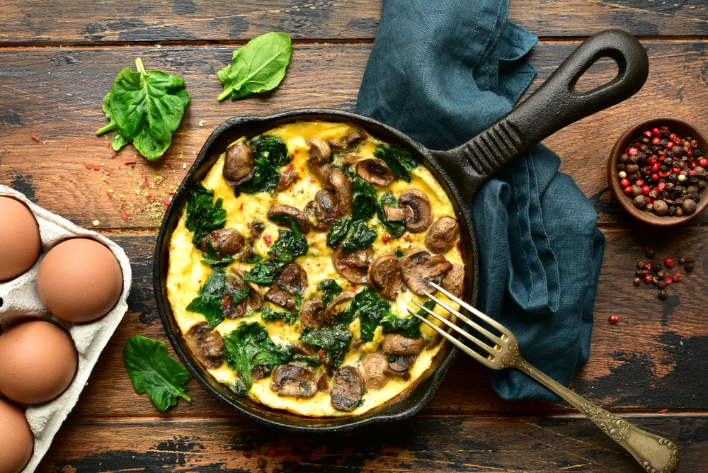 Omelette with mushrooms and spinach in a cast iron pan on a dark rustic wooden background.Top view with copy space.