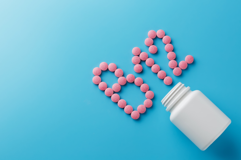 Pink round vitamins B12 shaped pills on a blue background spilled from a white can