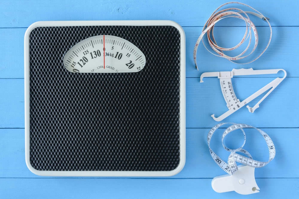 Mechanical weight scale, body mass control concept : Bathroom scale, personal accurate body fat tester / skin fold caliper measurement tool for stomach / belly and measuring tape on blue background
