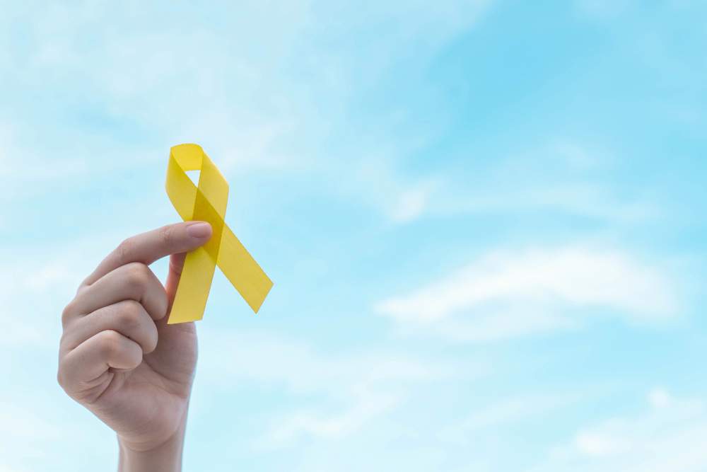 Hand holding yellow gold ribbon awareness over blue sky. Symbol for support suicide prevention, endometriosis, sarcoma bone cancer, bladder cancer, liver cancer and childhood cancer awareness concept.