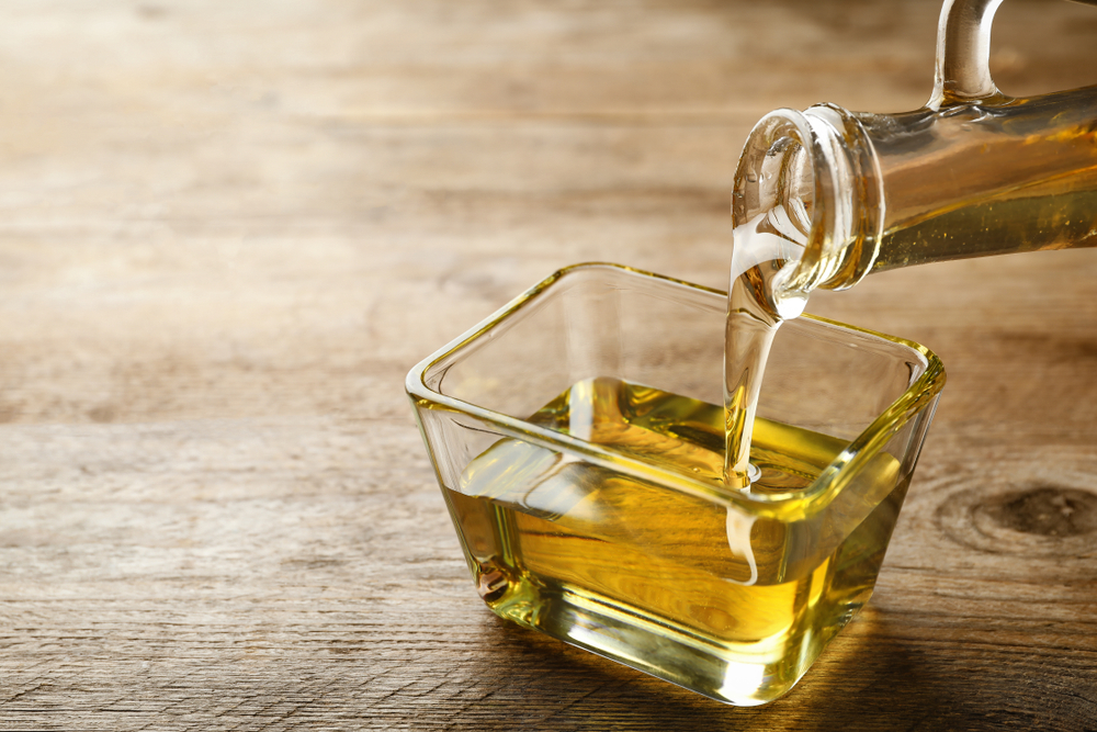 Pouring cooking oil from jug into bowl on wooden table
