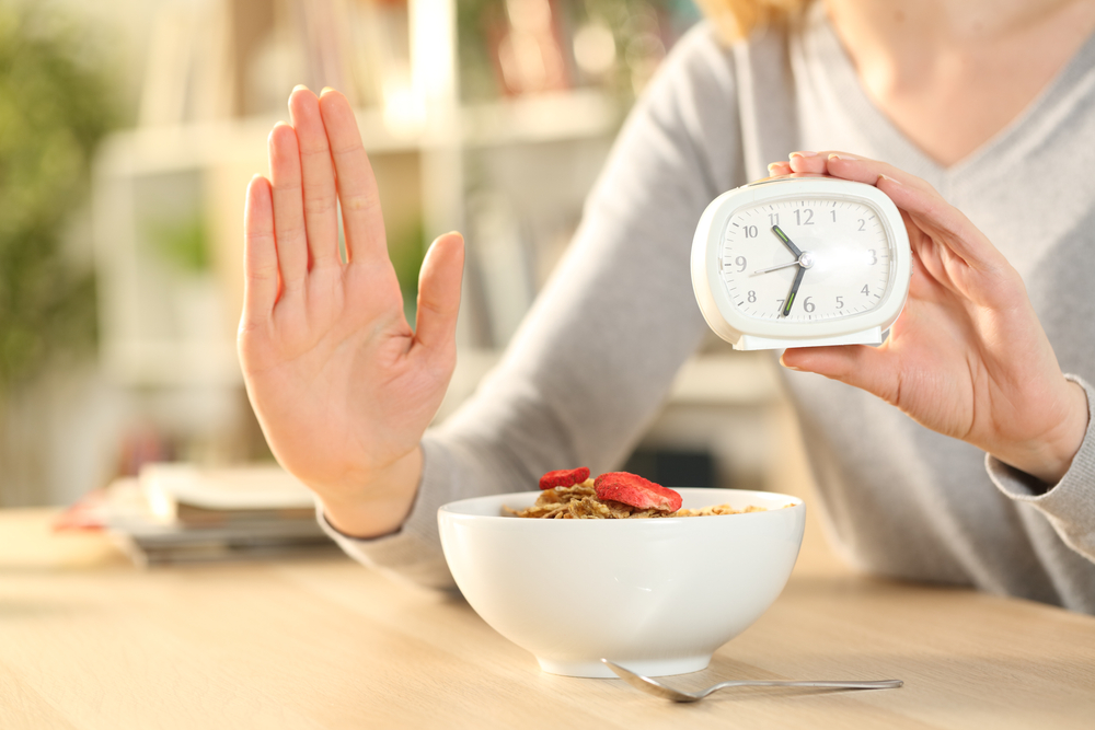 Close up of woman hands on intermittent fasting doing stop sign waiting before eating cereal bowl on a table at home