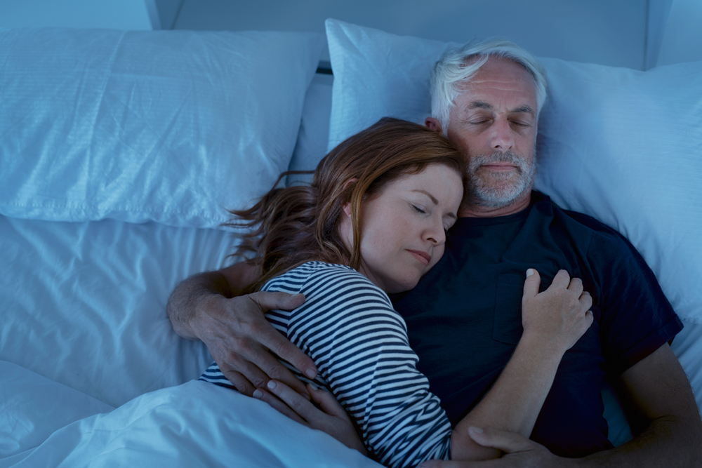 Senior man and woman sleeping and dreaming together in a deep sleep. Mature woman embracing and sleeps on her husband's chest while sleeping at night. Loving couple resting in their bed, copy space.
