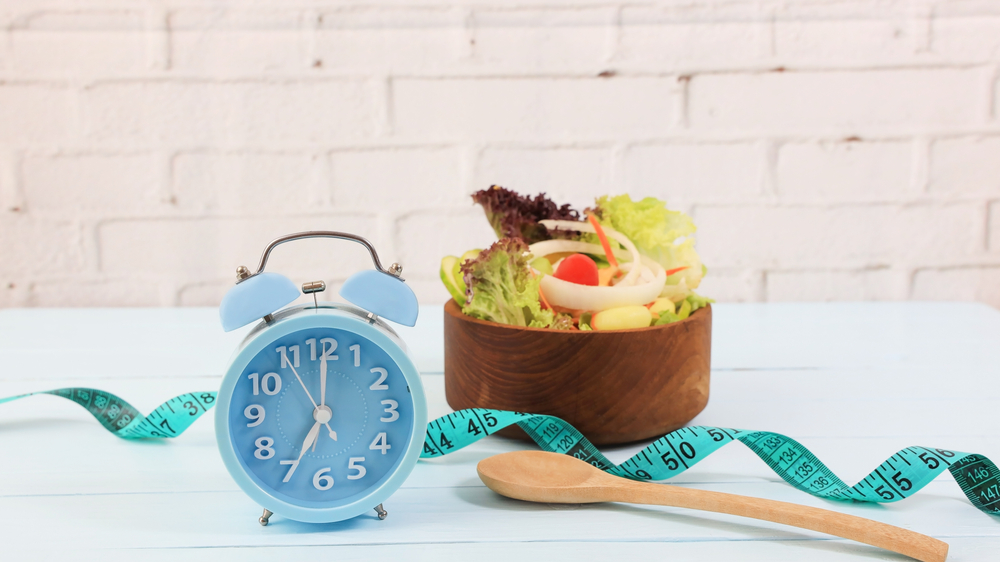 Selective focus Alarm of blue clock with Intermittent fasting and Healthy food and salad  as measuring tape for diet diary on wooden background