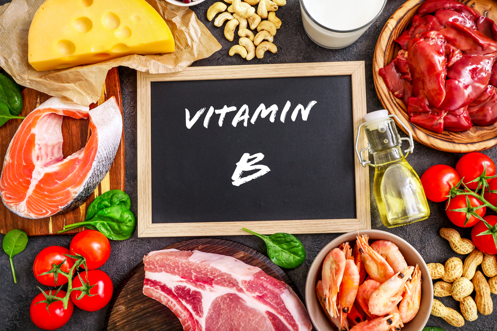 Assortment of high vitamin B sources on dark background: milk, liver, olive oil, tomatoes, prawns, peanuts, beef, spinach, salmon, keshew, cheese. Top view.